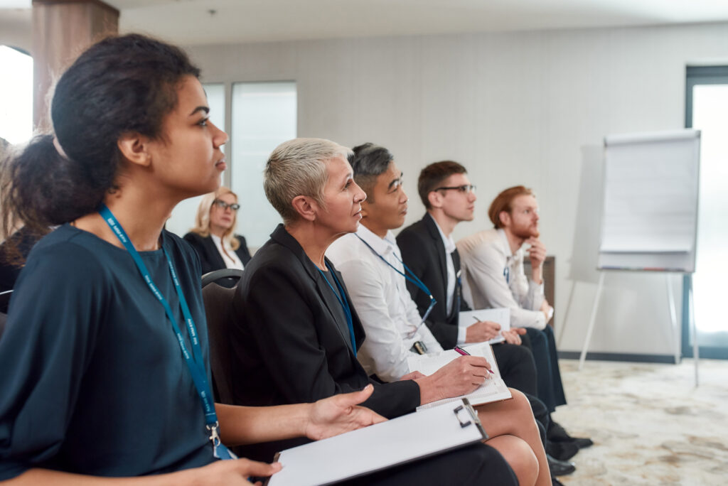 an audience in a training room listening to someone speaking off-camera