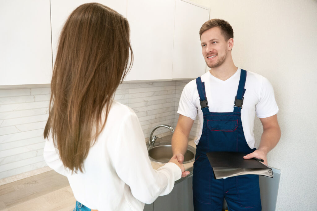 plumber and brunette woman client shaking hands after successful work on water tap installation professional repair service