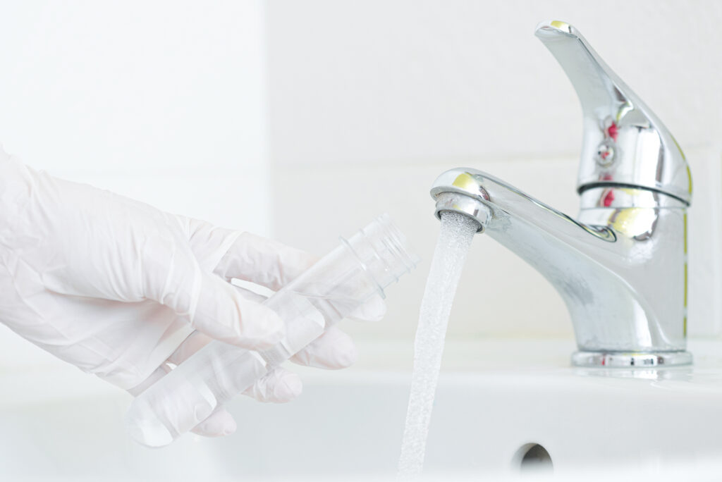 gloved hand using a closeable flask to take a water sample from a bathroom sink tap